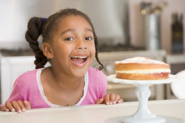 Young girl in kitchen looking at cake on counter smiling clipart