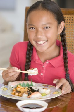 Young girl in dining room eating Chinese food smiling clipart