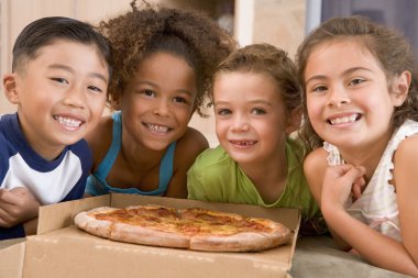 Four young children indoors eating pizza smiling clipart