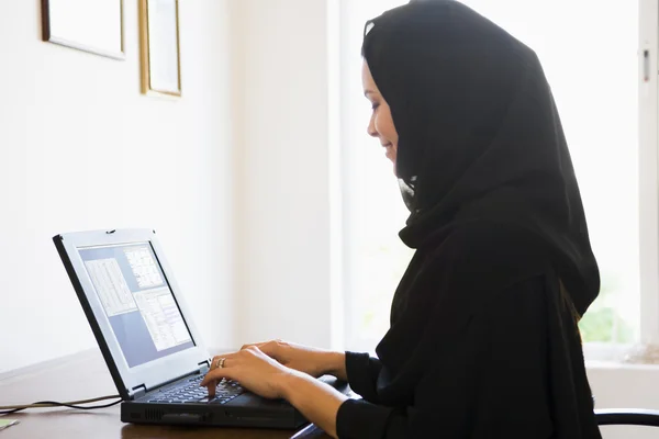 Uma mulher do Oriente Médio sentada na frente de um computador em casa — Fotografia de Stock