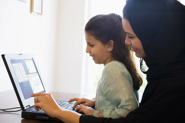 A Middle Eastern woman and her daughter sitting in front of a co — Stock Photo, Image