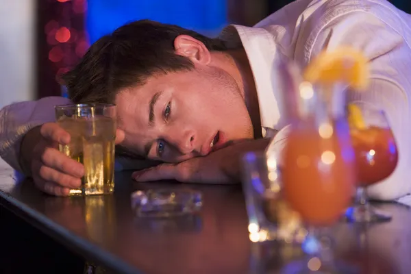 Пьяный молодой человек, лежащий головой на барной стойке — стоковое фото