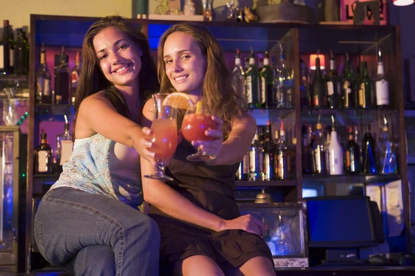 Zwei junge Frauen sitzen auf einem Tresen und prosten der Kamera zu — Stockfoto