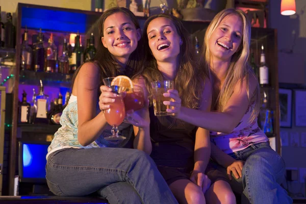 Três jovens mulheres sentadas num balcão de bar, a brindar à câmara — Fotografia de Stock