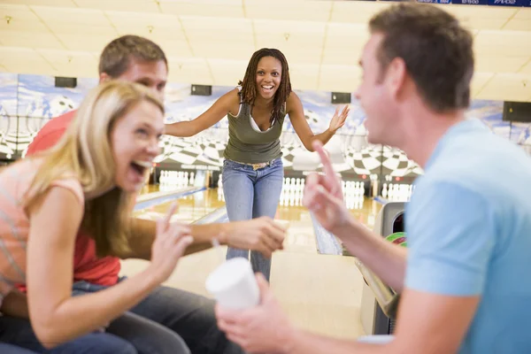 Four young adults laughing and gesturing in a bowling alley — Stock Photo, Image