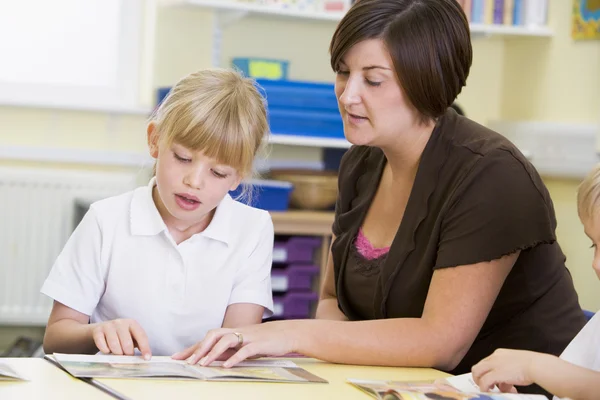 A schoolgirl and her teacher reading in a primary class — Stock Photo, Image