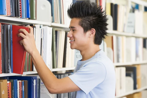 Estudiante universitario seleccionando libro del estante de la biblioteca — Foto de Stock