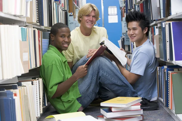 集团的三个男同学坐在图书馆的书被包围的地板上 — 图库照片