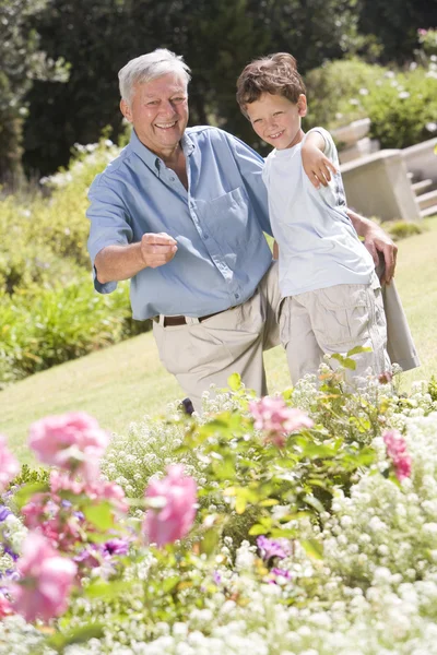 Grandfather and grandson outdoors in garden pointing at plants a — Stock Photo, Image