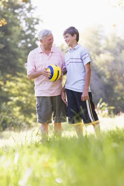 Grandfather and grandson at a park holding a ball and smiling — Stock Photo, Image