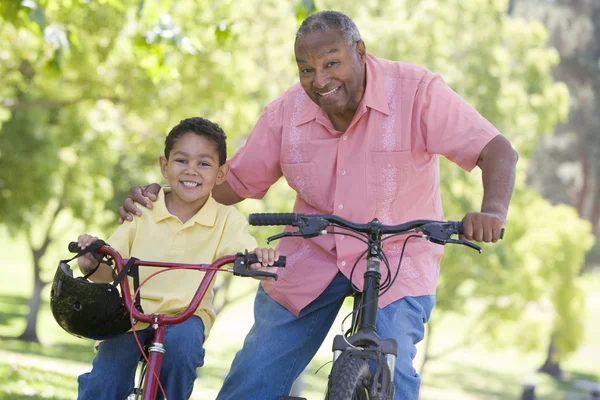Дедушка и внук на велосипедах на улице улыбаются — стоковое фото