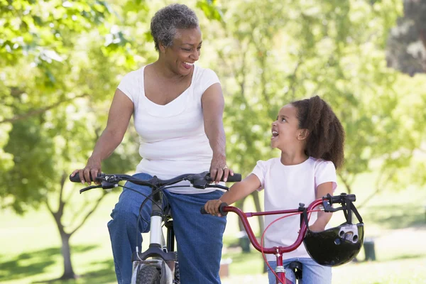Бабушка и внучка на велосипедах на улице улыбаются — стоковое фото
