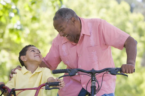 Opa und Enkel auf Fahrrädern im Freien lächelnd — Stockfoto