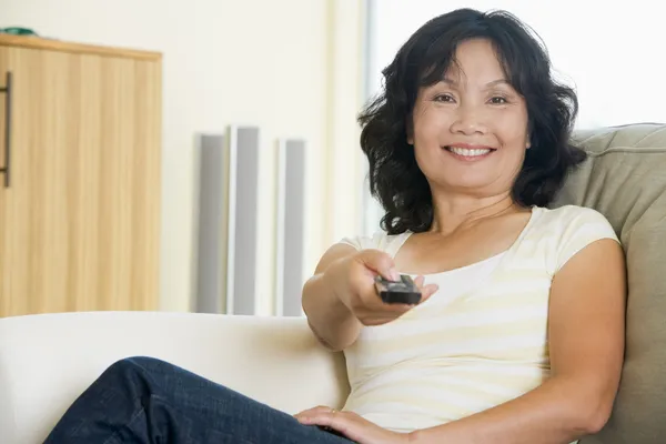 Женщина сидит в гостиной, держа пульт дистанционного управления улыбаясь — стоковое фото