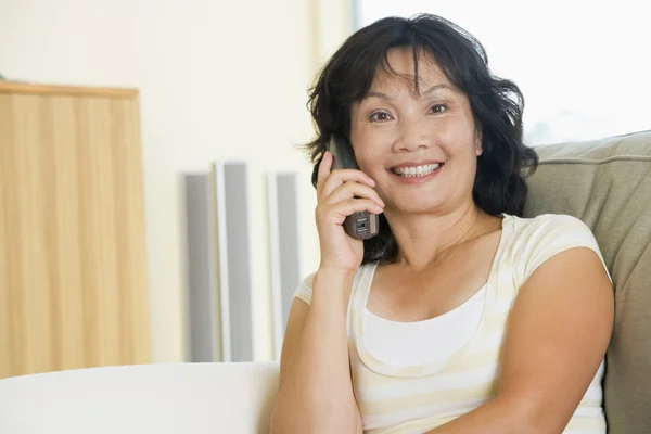 Frau sitzt mit Telefon im Wohnzimmer und lächelt — Stockfoto