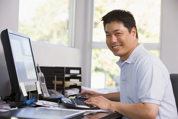 Чоловік в домашньому офісі використовує комп'ютер і посміхається — стокове фото