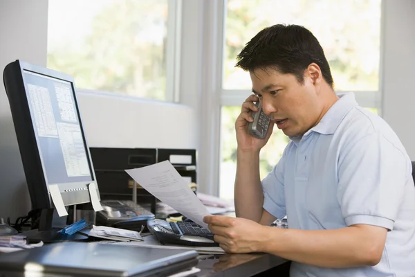 Человек в домашнем офисе с компьютером и бумажной работой по телефону — стоковое фото