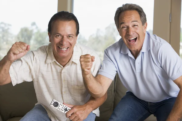 Двое мужчин в гостиной с дистанционным управлением веселятся и улыбаются — стоковое фото