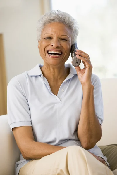 Mulher sentada na sala de estar usando telefone e sorrindo — Fotografia de Stock