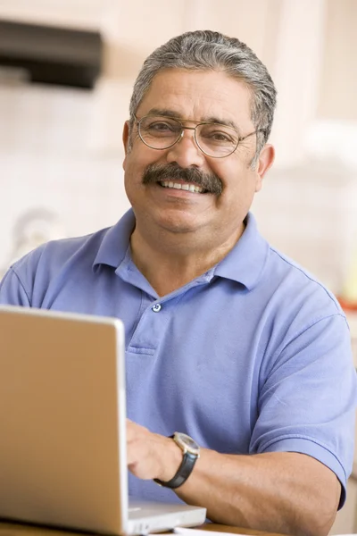 Człowiek w kuchni z laptopa uśmiechający się — Zdjęcie stockowe