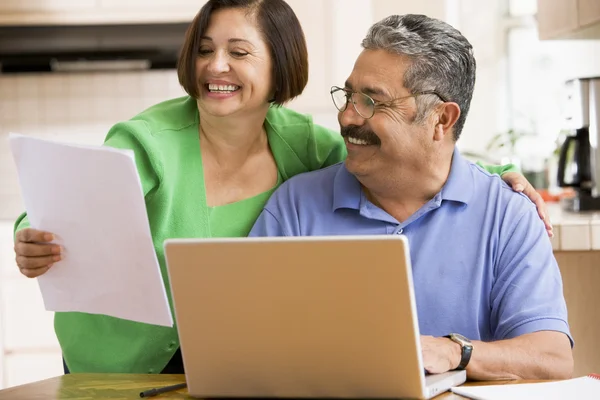 Paar in keuken met laptop en papierwerk glimlachen — Stockfoto