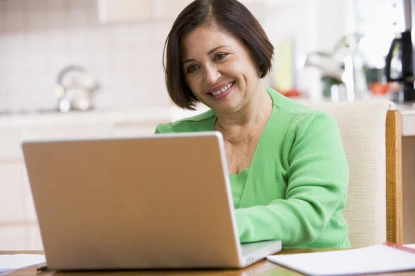 Женщина на кухне с ноутбуком улыбается — стоковое фото