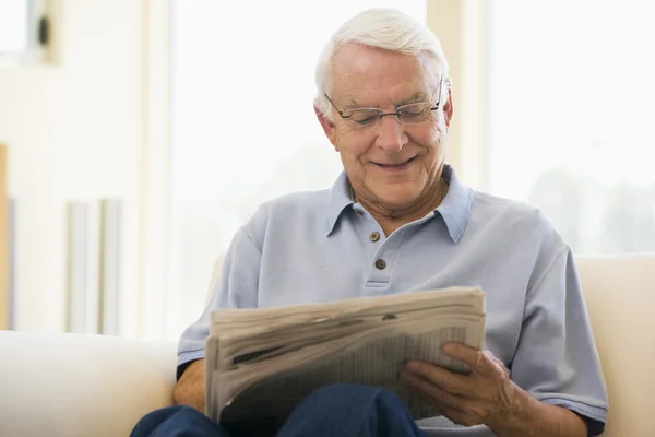 在客厅里读报纸微笑的男人 — 图库照片