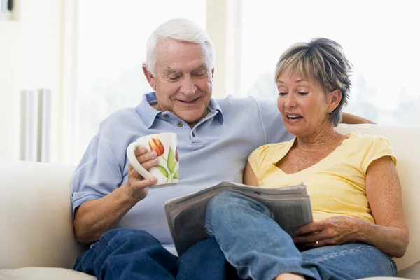 Пара в гостиной читает газету с улыбкой на лице — стоковое фото