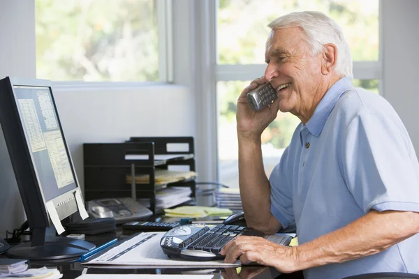 Mannen i hemma kontoret på telefon med datorn leende — Stockfoto