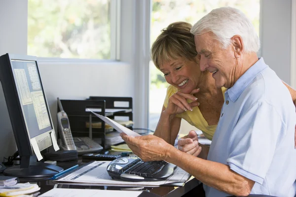 Couple in home office with computer and paperwork smiling — Stock Photo, Image