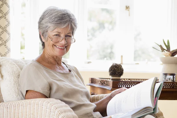 Vrouw in woonkamer lezen boek glimlachen — Stockfoto