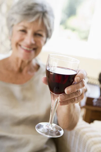 在客厅里与玻璃的葡萄酒微笑的女人 — 图库照片