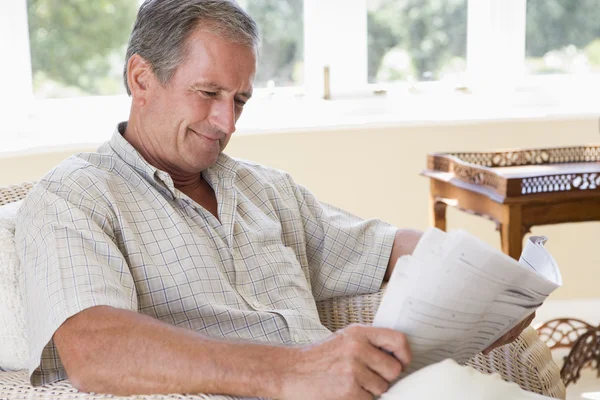 Человек в гостиной читает газету улыбаясь — стоковое фото