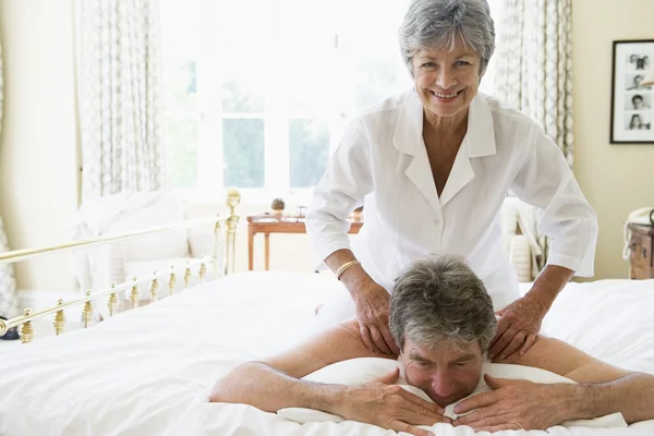 Mujer dando masaje de hombre en el dormitorio sonriendo —  Fotos de Stock