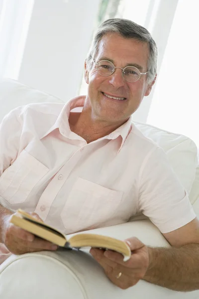 Man in woonkamer lezen boek glimlachen — Stockfoto