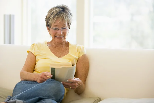 Mujer en la sala de estar leyendo libro sonriendo —  Fotos de Stock