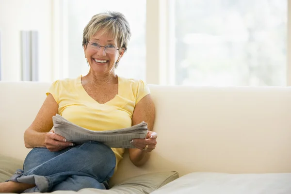 Vrouw in woonkamer lezen krant glimlachen — Stockfoto