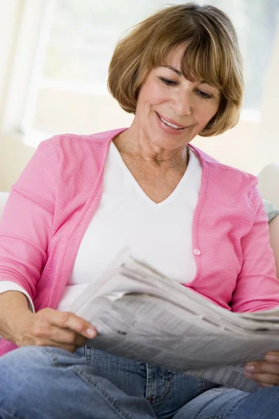 在客厅里读报纸微笑的女人 — 图库照片