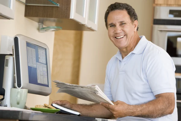 计算机和报纸微笑的厨房的男人 — 图库照片