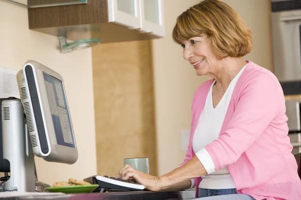 Mulher na cozinha com computador e café sorrindo — Fotografia de Stock