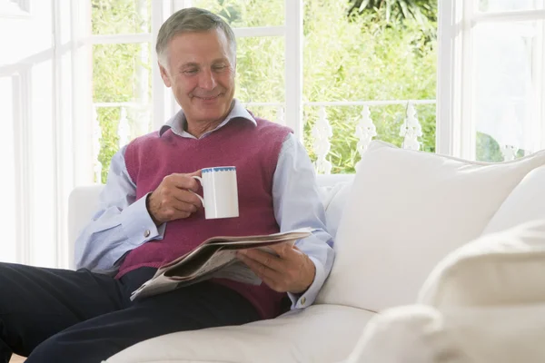 Mężczyzna w salonie z kawy, czytanie gazety uśmiechający się — Zdjęcie stockowe