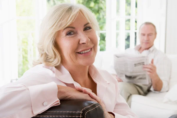 Женщина в гостиной улыбается с мужчиной на заднем плане, читая новости — стоковое фото