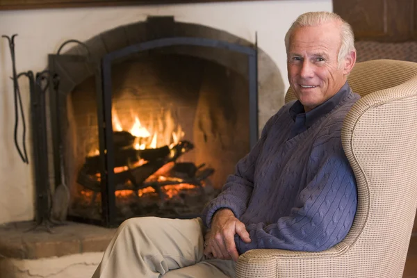 Hombre sentado en la sala de estar junto a la chimenea sonriendo — Foto de Stock