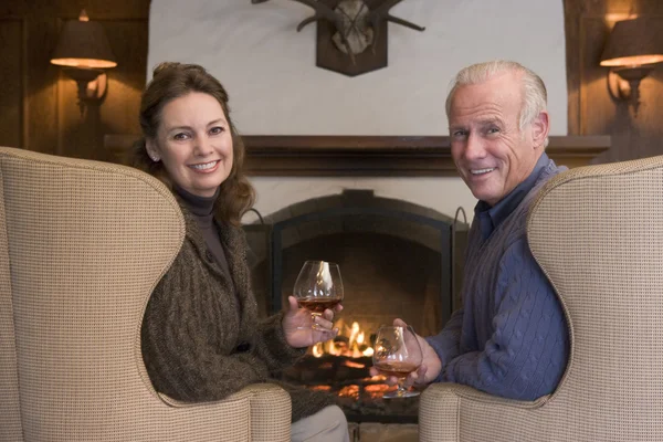 Пара сидить у вітальні біля каміна з напоями посміхаючись — стокове фото