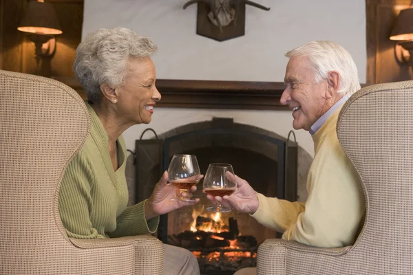Couple assis dans le salon avec cheminée et boissons souriantes — Photo