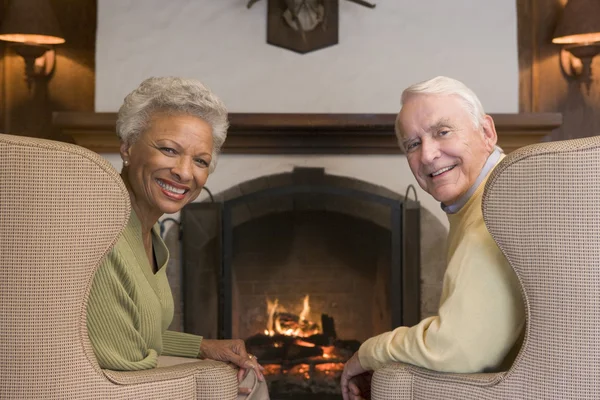 Couple sitting in living room by fireplace smiling — Stock Photo, Image