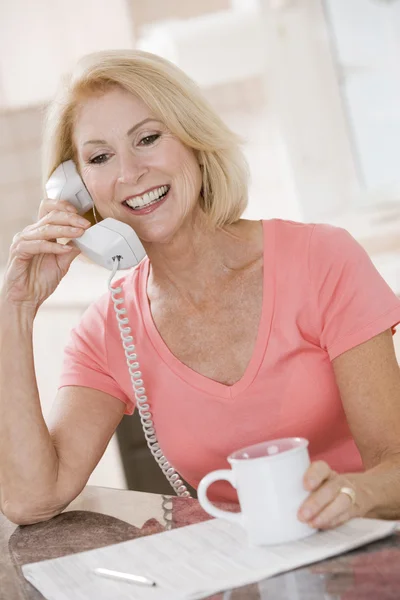 Frau in Küche mit Kaffee am Telefon lächelt — Stockfoto