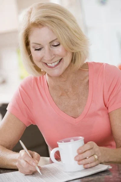 Donna in cucina con caffè e giornale sorridente — Foto Stock