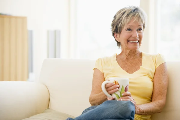 Frau entspannt sich im Wohnzimmer mit Kaffee lächelnd — Stockfoto