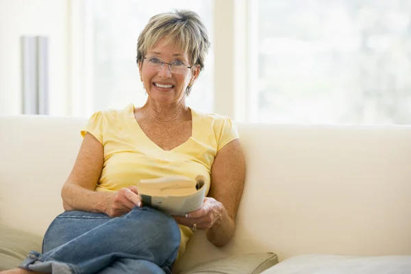 Mulher relaxante com livro na sala de estar e sorrindo — Fotografia de Stock